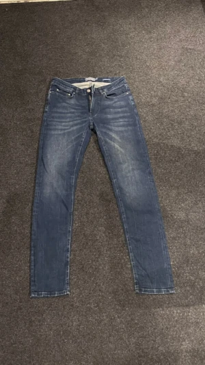 Blå jeans från Dressmann - Snygga blå jeans från Dressmann i klassisk straight fit. Jeansen har fem fickor, dragkedja och knapp framtill. Materialet är slitstarkt denim i bomull och passformen är normal. Perfekt för dig som gillar en enkel och stilren look.