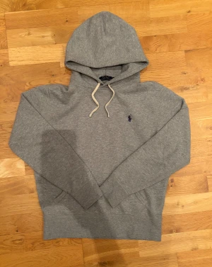 Grå hoodie från Polo Ralph Lauren - Snygg grå hoodie från Polo Ralph Lauren med klassisk broderad logga på bröstet. Tröjan har huva med vita snören, ribbade muddar och är tillverkad i mjuk bomull. Perfekt för chill dagar och enkel att matcha med jeans eller joggers. Kontakta mig vid minsta fundering✌🏻