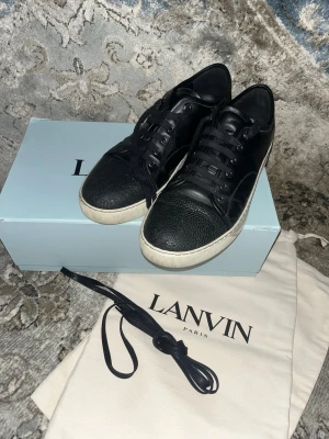 Svarta Lanvin sneakers i skinn - Lanvin sneakers i svart skinn med texturerad tå och vita platta sulor. Klassisk rund tå, svarta snören och metallöglor. Snygg minimalistisk design med exklusiv känsla, perfekt för dig som gillar stilrena och lyxiga sneakers. Endast smutsiga undantill annars jätte rena. Använt dom kanske 4 gånger själv för massa år sedan och har bara legat i lådan sen dess. Priset kan sänkas vid en snabb affär. För fler frågor eller funderingar är det bara att höra av sig MVH
