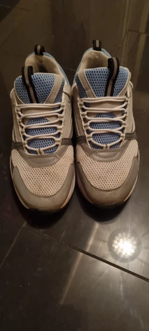  B22 - Chunky sneakers i grått och blått med vit mesh och detaljer i syntetmaterial. Skorna har snörning och en platt, bred sula som ger en cool streetstil. Ventilerande mesh på ovansidan och svarta dragflikar på plösen för extra edge. Perfekta för dig som gillar sportig vibe.