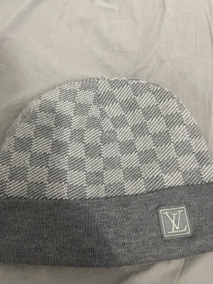 Grå rutig mössa  - Snygg grå mössa med rutigt mönster och uppvikt kant.  Stickad i mjukt material som känns lyxigt och passar perfekt när det är kallt ute. Diskret och stilren design som lyfter din look.