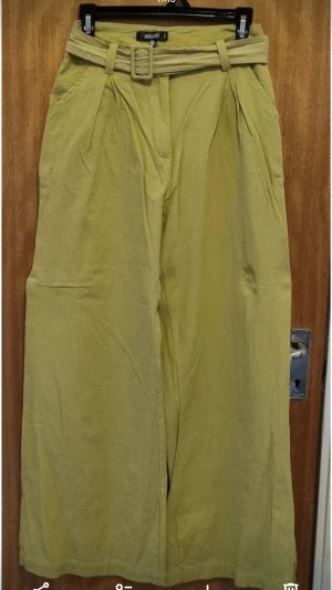 Beige linnebyxor från Missguided - Snygga beige linnebyxor från Missguided med breda ben och hög midja. Byxorna har ett matchande bälte i samma material och mjuk struktur. Perfekta för en chill och trendig look.