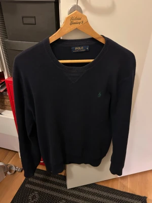 Mörkblå stickad tröja Ralph Lauren - Snygg mörkblå stickad tröja från Polo Ralph Lauren i storlek S. Klassisk rund halsringning och diskret grön logobrodering på bröstet. Perfekt för dig som gillar stilrena och tidlösa plagg med en soft vibe. Underbart skick perfekt till vinter och kallare dagar!