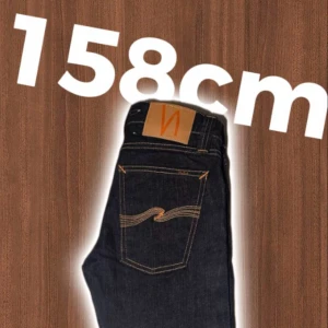 Mörkblå jeans från Nudie Jeans - Snygga mörkblå jeans från Nudie Jeans med klassisk femficksdesign och kontrastsömmar. Modellen har raka ben och normal passform, med detaljerad broderad logga på bakfickan och läderpatch i midjan. Perfekt för dig som gillar stilrena och tidlösa jeans.