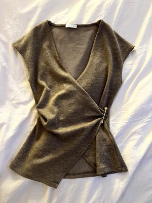 Brun/beige omlottopp från Zara - Säljer en brun/beige omlottopp från Zara med v-ringning och korta ärmar. Toppen har en snygg detalj med guldfärgad pin i sidan som håller omlottstilen på plats. Den här är aldrig andvänd!