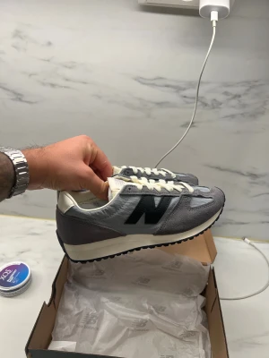 Grå New Balance 237 sneakers strl 37 -  New Balance  sneakers i grå mocka och textil med svarta detaljer och vit sula. Klassisk retrostil med rund tå, platt sula och vita snören. Perfekta för dig som gillar stilrena och bekväma sneakers med en sportig vibe.