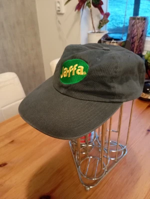 Ny Jaffa keps  - Säljer en grön keps med broderad Jaffa-logga i gult och grönt framtill. Kepsen har klassisk form med böjd skärm och är tillverkad i slitstark bomull. Perfekt för dig som gillar retro och vill sticka ut med en unik accessoar.