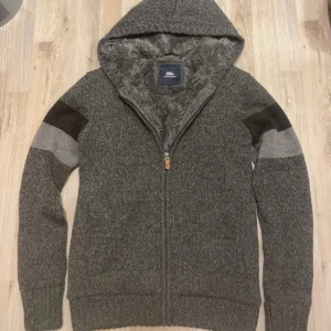 Grå fodrad stickad cardigan - Otroligt snygg grå och svart fodrad stickad cardigan i toppskick. Passar perfekt nu till kallare väder. Storlek L men sitter mer som en M.  Armhåla- armhåla är 47 cm ungefär. Axel till midja är 67cm ungefär Bara att höra av sig vid frågor och funderingar. Priset kan såklart diskuteras!