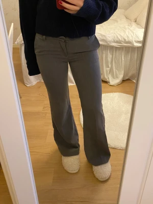 Grå bootcut kostymbyxor - Snygga grå kostymbyxor med bootcut passform och klassiska fickor fram och bak. Byxorna har låg midja och stängs med dragkedja och hylsa. Passar mig som är 163 och längre. 