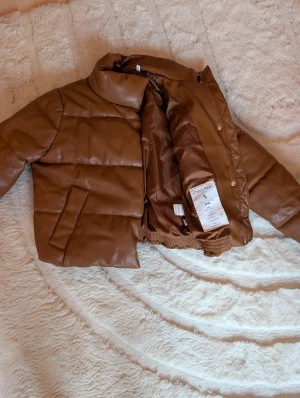 Brun pufferjacka från Calvin Klein - Säljer en brun pufferjacka från Calvin Klein i storlek M. Jackan har hög krage, två sidofickor och stängs med dragkedja och tryckknappar. Yttermaterialet är syntet med en mjuk känsla och quiltad design. Perfekt för kalla dagar och riktigt snygg till streetwear.