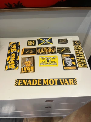 Norra Stå - AIK supporterklistermärken - Samling med AIK-inspirerade klistermärken i svart och gult. Perfekt för dig som vill visa ditt stöd på matchen, i vardagen eller på prylar. Motiv som 'Norra Stå', 'Enade mot VAR', 'Frihet för Ultras' och flera AIK-profiler. Skapa din egen supporterstil!
