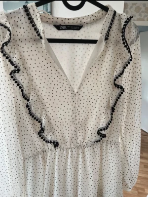 Prickig volangklänning från Zara - Supersöt vit kortklänning från Zara med svarta prickar och volangdetaljer längs v-ringningen och kjolen. Klänningen har långärmade ärmar. Den är i fint skick!🖤🤍