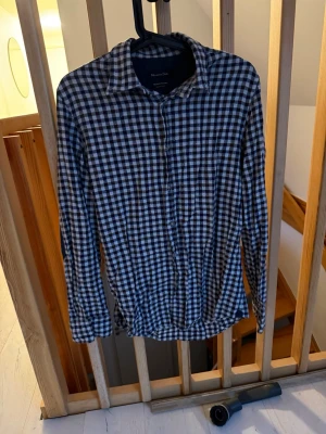 Rutig skjorta från Massimo Dutti - Snygg rutig skjorta från Massimo Dutti i svart och beige med klassisk krage och knappar framtill. Skjortan har lång ärm med mörkgrå armbågslappar i fiskbensmönster. Tillverkad i mjuk bomull, perfekt för dig som gillar stilrena detaljer.