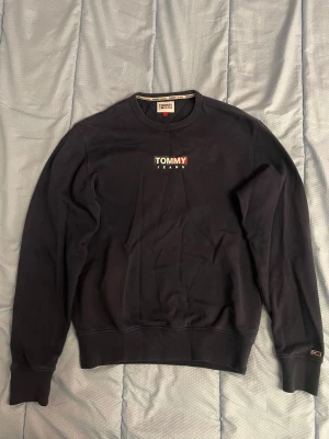Mörkblå tröja, Tommy Jeans storlek S - Hej, jag säljer en mörkblå tröja från Tommy Jeans i storlek S men jag skulle säga att den är stor i storleken så egentligen är det storlen M. Tröjan har varit använd ganska ofta men är i väldigt bra skick ändå. Tröjan är skön och varm och sitter bra på kroppen. 