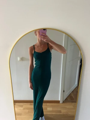 Mörkgrön långklänning med smala axelband - Säljer en mörkgrön långklänning med smala axelband & figurnära passform. Materialet känns mjukt & följsamt mot kroppen, superskön att ha på sig. Klänningen är ifrån Boohoo & i storlek XS