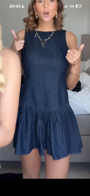 Mörkblå ärmlös kortklänning - Supersöt mörkblå kortklänning med ärmlös design och volangkjol. Klänningen har en enkel rund halsringning och är sydd i ett lätt material som ger en avslappnad och flowy känsla. Perfekt för dig som gillar en stilren men ändå lekfull look.