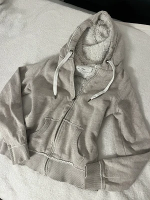 Beige hoodie med fluffigt foder L.O.G.G. - Mysig beige hoodie från L.O.G.G. med fluffigt vitt foder på insidan och i huvan. Dragkedja framtill, två fickor och ribbade muddar. Snygga vita snören i huvan och detaljer i metall. Perfekt för chill dagar och extra värme.