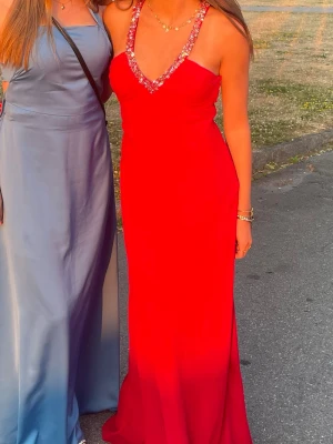 Röd balklänning/ långklänning  - Säljer min fina balklänning som jag älskar!  djup v-ringning och glittriga paljetter längs halsringningen. Klänningen har öppen rygg med dekorativa ringar och smala axelband. Passformen är figurnära och tyget faller snyggt längs kroppen. Klänningen är lång och går såklart att läggas upp 