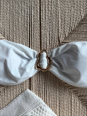Vit bandeau tubtopp med gulddetalj - Säljer en vit bandeau bikini tubtopp med snygg guldfärgad metallring i mitten. Toppen har knytning baktill för att justera passformen. Materialet är mjukt och stretchigt. Inte kommit till användning 