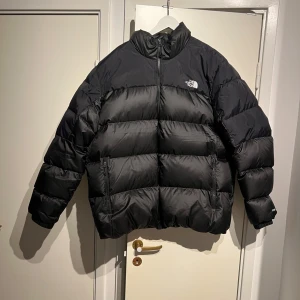 Svart dunjacka The North Face 700 - Säljer en klassisk The North Face Nuptse 700 i svart, storlek XXL. Jackan är köpt förra vintern för cirka 3700 kr och har endast använts en gång – den är i absolut nyskick.  Det här är en av de mest populära vinterjackorna från The North Face. Nuptse är känd för sin stilrena design, rejäla värme och höga komfort. Den fungerar lika bra i stan som under kalla vinterdagar utomhus.  Material: 	•	Yttermaterial: 100 % nylon (ripstop, slitstarkt och vattenavvisande) 	•	Fyllning: 700-fill gåsdun (90 % d