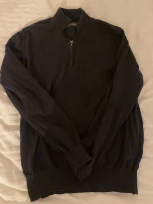 Mörkblå stickad half zip från Oscar Jacobson - Snygg mörkblå stickad tröja från Oscar Jacobson med half zip och hög krage. Tröjan har långärmade ribbade muddar och är perfekt för dig som gillar stilren och klassisk design. Passar dig som vill ha en enkel men ändå sofistikerad look.