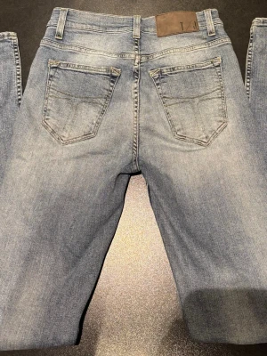 Ljusblå jeans Tiger of Sweden 29/34 - Snygga ljusblå jeans från Tiger of Sweden i klassisk femficksmodell. Jeansen har raka ben, normal passform och är tillverkade i mjukt denimtyg med subtila slitningar. Passar dig som gillar en enkel och tidlös look. Storlek 29/34