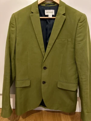 Snygg olivgrön kavaj från H&M Conscious / (PREMIUM SELECTION) - Snygg olivgrön kavaj från H&M Conscious Collection ( passar mer som M/L) med två knappar framtill, klassisk krage och fickor med lock. Lätt och stilren modell i bomullsblandning, perfekt för dig som vill sticka ut med färg. Fodrad insida och långa ärmar.