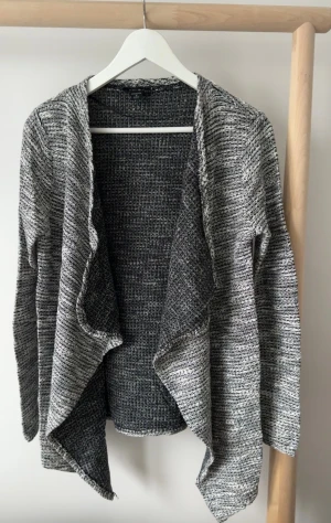 Gråmelerad kofta från New Yorker - Säljer en gråmelerad, öppen kofta från New Yorker i storlek M. Koftan har lång ärm, mjukt stickat material och en avslappnad, loose passform med snyggt fall framtill. 