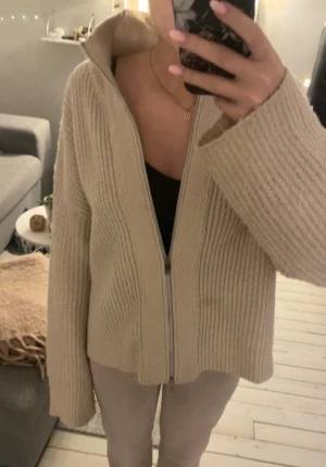 Beige stickad kofta med dragkedja 157 - Mysig beige stickad kofta från 157 i storlek S. Koftan har en ribbad struktur, långärmade ärmar och en hel dragkedja framtill. Perfekt för lager-på-lager och chill dagar💞