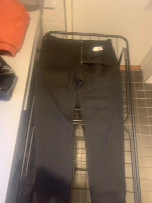 Svarta tapered byxor från Gabba - Snygga svarta byxor från Gabba med tapered passform och klassisk dragkedja fram. Byxorna har bälteshällor och en stilren look som funkar till många olika outfits. Materialet är mjukt och följsamt, perfekt för dig som gillar en modern siluett.