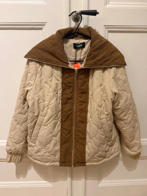  Beige jacka med brun krage från Cider - Oanvänd jacka från Cider i beige med breda bruna manchesterdetaljer på krage och mitt fram.