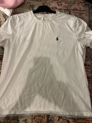 Vit t-shirt Polo Ralph Lauren slim fit - Vit t-shirt från Polo Ralph Lauren i slim fit-modell. Klassisk rund hals och korta ärmar, med den ikoniska mörkblå Polo-loggan broderad på bröstet. Tillverkad i mjuk bomull som känns skön mot huden. Perfekt för en clean och stilren look.