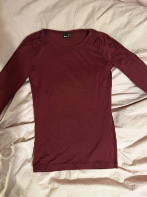 Vinröd topp från Gina Tricot - Säljer en enkel och stilren vinröd långärmad topp från Gina Tricot.  Materialet är mjukt och stretchigt, perfekt för att styla med jeans eller kjol. Toppen är enfärgad och har en klassisk look.