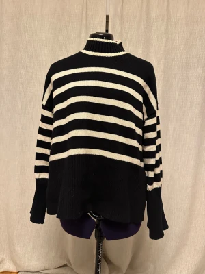 Svartvit randig stickad tröja JJXX - Säljer en svart och vit stickad tröja från JJXX med breda ränder och hög ribbad krage. Tröjan har långärmade ärmar med extra breda muddar och en loose passform. Perfekt för dig som gillar en chill och trendig look.