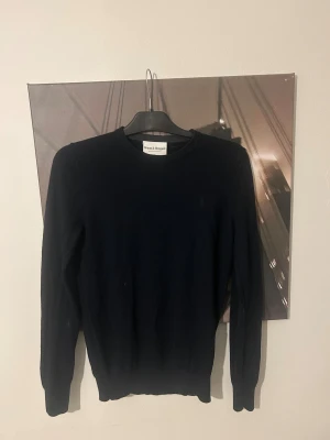 Svart stickad tröja Bruun & Stengade - En stilren svart stickad tröja från Bruun & Stengade i storlek S. Tröjan har rund halsringning och långa ärmar, perfekt för lager-på-lager under kyliga dagar. Enkel och klassisk design som funkar till många olika outfits.