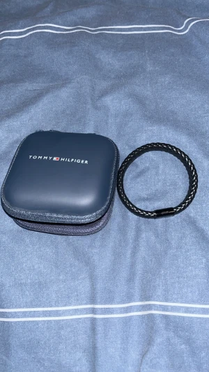 Armband - Säljer ett Tommy Hilfiger Round Braided Bracelet i svart. Armbandet är gjort i flätat läder med magnetiskt metallspänne och Hilfiger-loggan. Det är i bra skick med endast små repor från normalt användande. Nypris ca 779 kr.   Perfekt accessoar för dig som gillar en stilren och tidlös look.