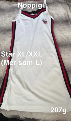 Vit sportig klänning Miss Shilly - Vit ärmlös klänning från Miss shilly med svarta och röda ränder längs sidorna och broderad logga på bröstet. Klänningen har smala axelband och en sportig look, perfekt för en avslappnad stil. 🌸 Noppig. Står XL/XXL men upplever mer som L