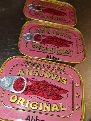 Grebbestads Ansjovis Original Abba - Säljer tre burkar Grebbestads Ansjovis Original från Abba. Burkarna har en snygg retrodesign i rosa och gult med illustration av röda fiskar och stjärnor. Metallburk med praktisk öppningsring, perfekt till klassiska rätter eller som cool köksdetalj.