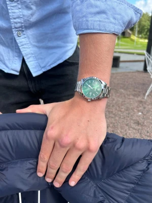 Grön klocka från Doventi med metallarmband - Snygg klocka från Doventi med grön urtavla och stilrena vita detaljer. Klockan har ett robust silverfärgat metallarmband och rund boett. Urtavlan har datumvisning och minimalistiska indexmarkeringar. Perfekt accessoar för dig som vill sticka ut med en cool färg på handleden.