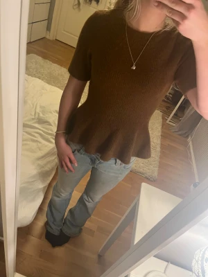 Brun stickad topp med volang från H&M - Säljer en brun stickad topp från H&M i storlek S. Modellen har korta ärmar, rund hals och en snygg volangkant nedtill. Använd ca 3 gånger och säljs för att den inte blir använd