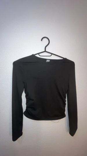 Svart croppad långärmad topp Shein - Svart långärmad topp från Shein i croppad modell. Tunn och mjuk polyester med lätt rynkade sidor för en snygg passform. Enkel design med rund hals och smala ärmar, perfekt för dig som gillar stilrena plagg. Det är tre samma men i olika färg baby blå grå och svart 