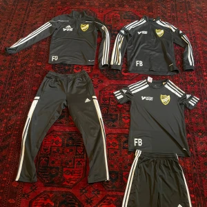 Träningsset från Adidas i storlek 152 / 11-12 år - Träningskläder från Adidas, inklusive träningströja, överdragströja, överdragsbyxor, tränings T-shirt och träningsshorts. Allt är i svalt funktionsmaterial med god andningsförmåga. På tröjorna finns klubbemblemet av den anrika klubben IFK Hässleholm. Flera av plaggen är i nyskick. 