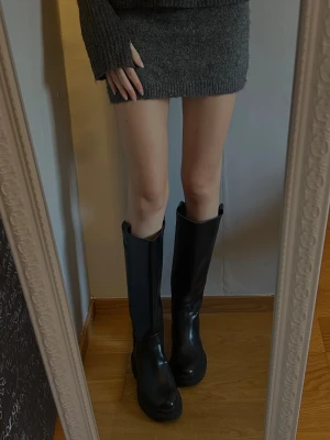 Svarta höga boots i skinn - Snygga boots/stövlar från HM. Endast använd en gång. De är snygga att styla till en klänning eller som på bilderna en kjol. Men går även att använda mer vardagligt. 