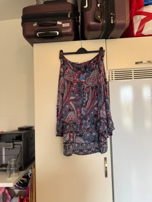 Mönstrad kortkjol med knappar - Snygg kortkjol med färgstarkt paisleymönster i blått, rött och beige. Kjolen har volangkant nedtill och dekorativa knappar framtill. Materialet är lätt och luftigt, perfekt för varmare dagar. Passformen är normal och kjolen har en skön flowy känsla. Från märket Odd Molly. Storlek 3 som enligt deras storleksguide motsvarar en L. Mycket fint skick, jag hittar inga synliga anmärkningar eller defekter. 