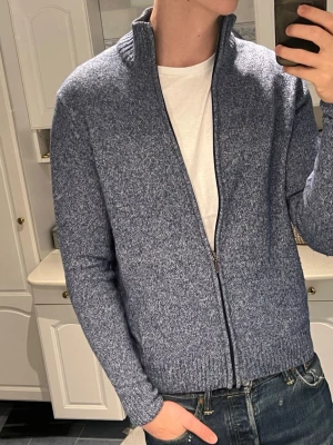 Blå full zip i Lammull  - Snygg blåmelerad kofta med ståkrage och hel dragkedja framtill. Tröjan har ribbade muddar vid ärmslut och nederkant, samt långärmad passform. Perfekt att slänga på över en t-shirt för en chill och stilren look. Den k är 80% Lammull fraktar inom 24 timmar✅📬