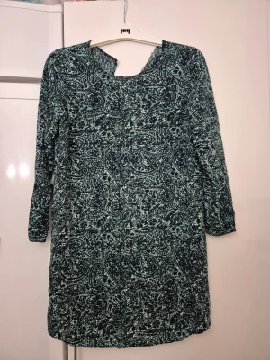 Klänning - Snygg klänning från Jacqueline de Yong i storlek 38. Klänningen har ett mörkblått och vitt mönster, långärmad design och v-ringad hals. Materialet är mjukt och lätt, perfekt för dig som gillar att sticka ut med coola prints.