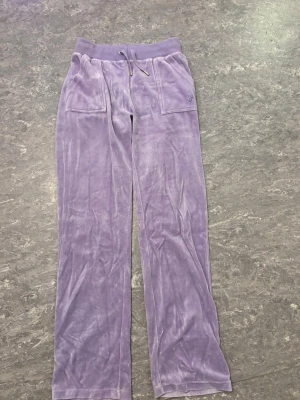 Lila juicy couture byxor  - Snygga lila mjukisbyxor från Juicy Couture i mjuk velour med bred resår och snörning i midjan. Perfekta för chill och streetwear.