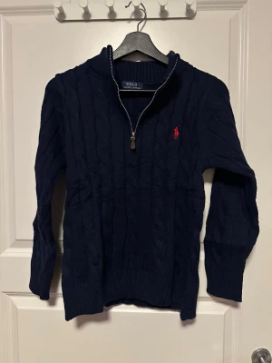 Knitwear från Polo Ralph Lauren - Mörkblå Knitwear från Polo Ralph Lauren med klassisk rund hals och lång ärm. Diskret röd Polo-logga broderad på bröstet. Mjuk och skön ullskvalitet, perfekt för chill dagar. Stilren och enkel design som funkar till jeans.