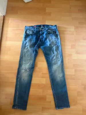 Replay Anbass blå slitna jeans - Säljer ett par Replay Anbass jeans i blå tvätt med slitningar och hål på benen för en riktigt avslappnad och trendig look. Klassisk femficksmodell med skinny passform och snygga detaljer. Perfekta för dig som gillar streetstyle och vill ha ett par jeans med attityd.