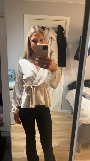 Beige omlottblus med knytband - Snygg beige omlottblus med knytband i midjan och volang nertill från missay. Blusen har långa ärmar med resår vid handlederna och är gjord i ett glansigt, mjukt tyg som ger en lyxig känsla. Nypris 300 säljer 180